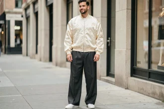 Homme en look RnB 2026 avec bomber satiné crème et pantalon large charbon en rue urbaine